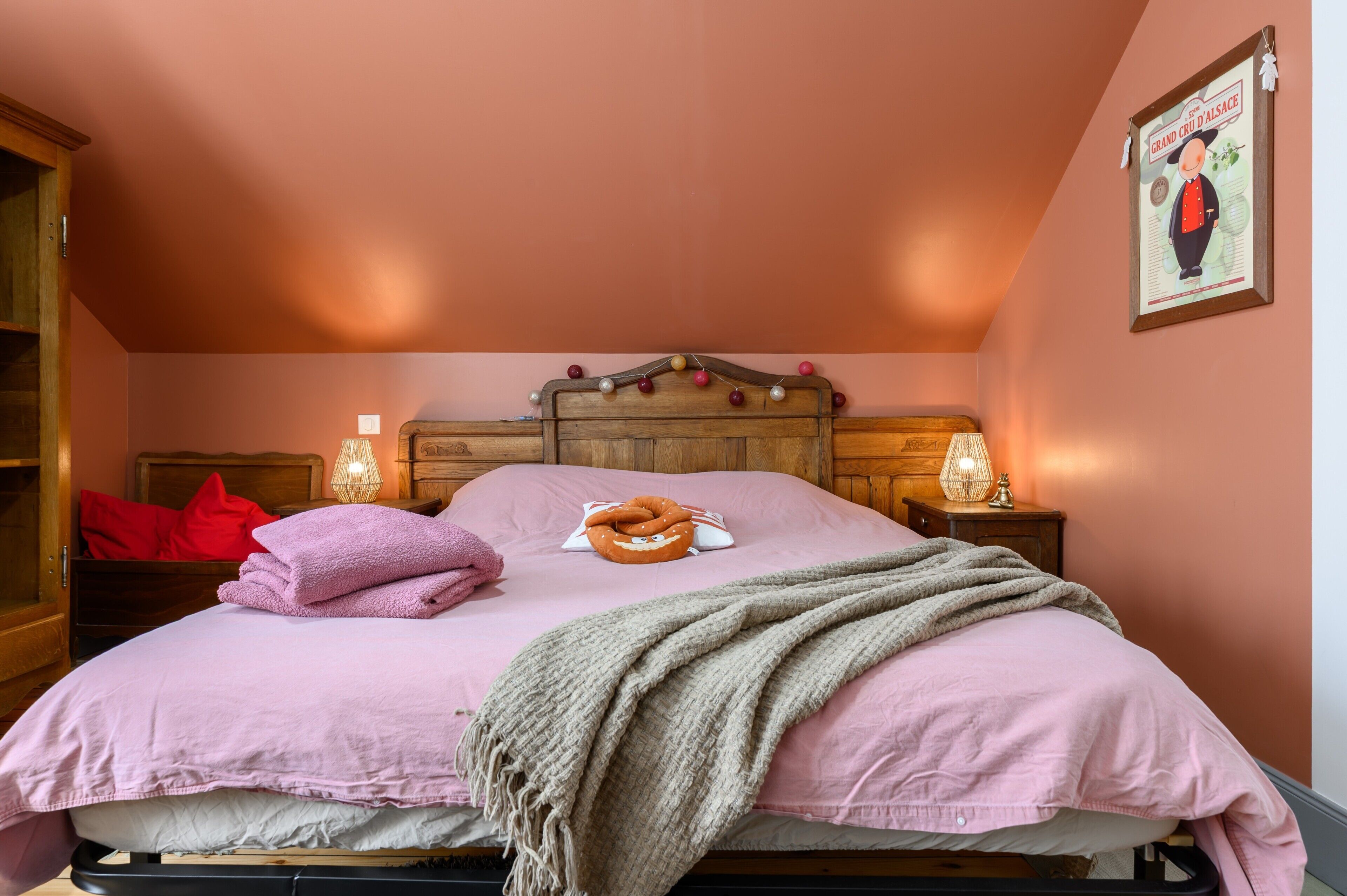 Une chambre à coucher avec un lit, des oreillers, une couverture, des lampes de chevet et une affiche accrochée au mur.