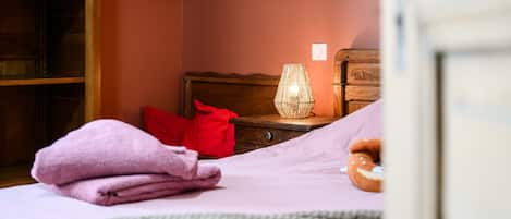 A bedroom with a bed, a nightstand, a lamp, and a wooden wardrobe.
