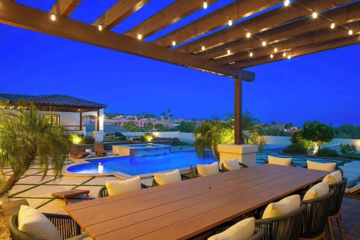 An outdoor pool area with a wooden pergola, lounge chairs, and a dining table.