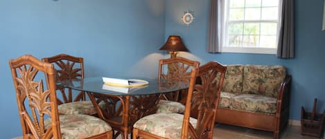 A dining area with a round glass table, four chairs, a sofa, a lamp, and a window with curtains.