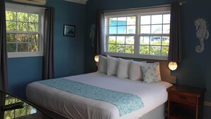 Une chambre à coucher avec un lit, deux fenêtres, une table de chevet et une lampe fixée au mur.