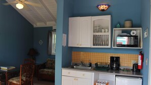 Une cuisine compacte avec des meubles blancs, un four à micro-ondes, une machine à café et un extincteur.