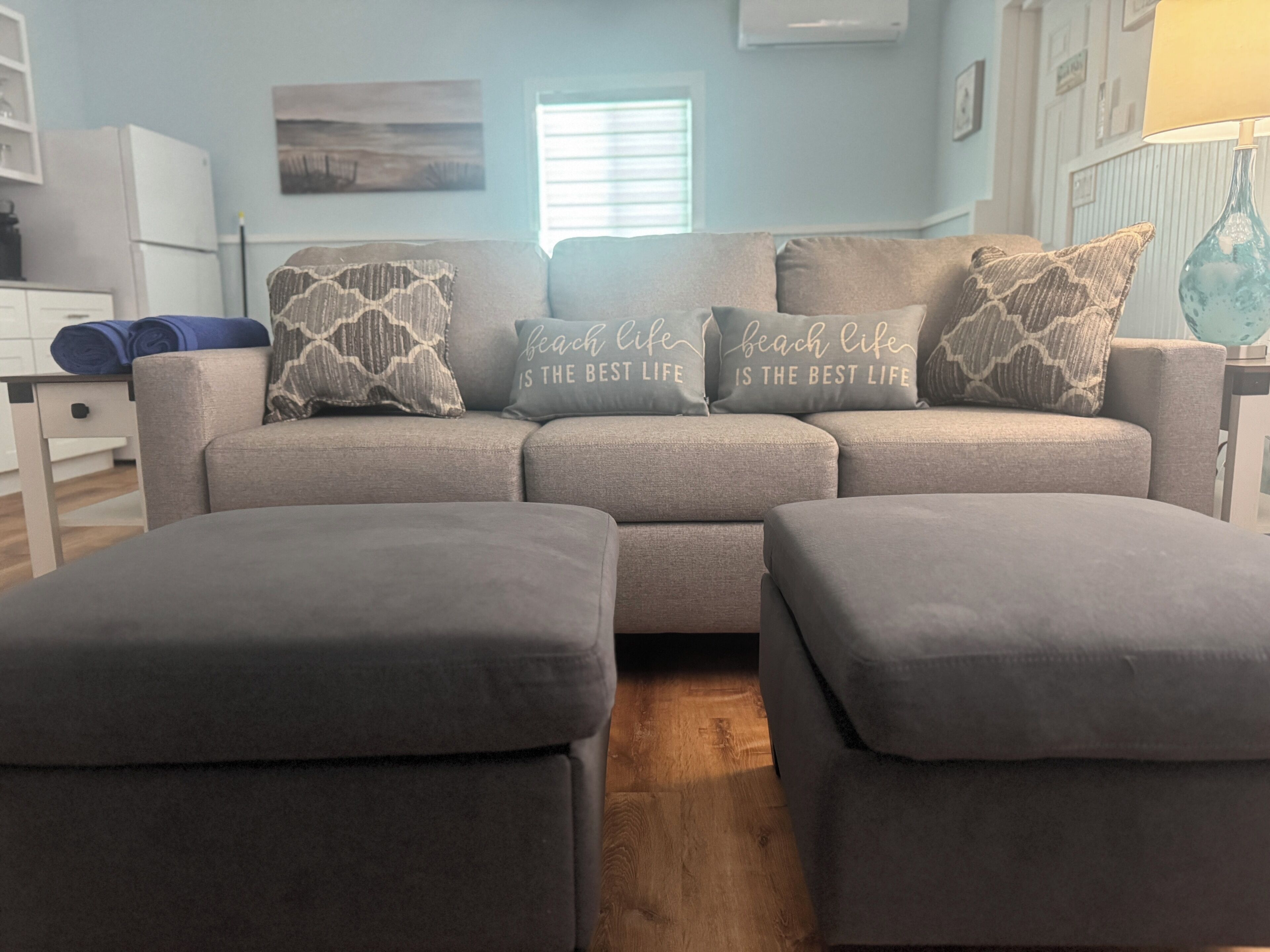 A living room with a grey sofa, matching ottomans, and decorative pillows with text.