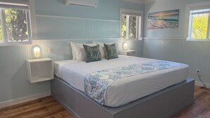 Une chambre à coucher avec un grand lit, deux tables de chevet, un climatiseur et un tableau au mur.