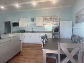 A compact kitchen with white cabinets, a dining table, and chairs. There is a microwave, toaster, and sink. - BEACHSIDE TWO BEDROOM VILLA - PARTIAL OCEAN VIEW (Georgetown)