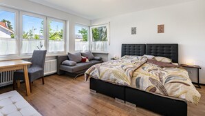 A bedroom with a bed, a desk, a chair, a sofa, and a window.