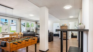 A modern living room with a foosball table, a sofa, and a dining area with chairs.