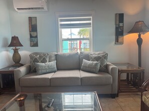 Ein Wohnzimmer mit einer Couch, einem Glastisch, einer Lampe und einem Fenster mit Blick auf Gebäude.