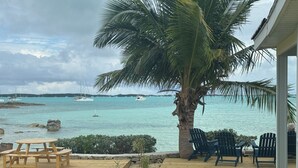 A wooden deck with chairs, a table, a palm tree, and a view of the sea with boats. - BEACHSIDE TWO BEDROOM VILLA - OCEANVIEW (Georgetown)