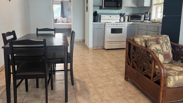 A kitchen with white cabinets, a microwave, stove, and a dining area with a table and chairs. - BEACHSIDE TWO BEDROOM VILLA - OCEANVIEW (Georgetown)