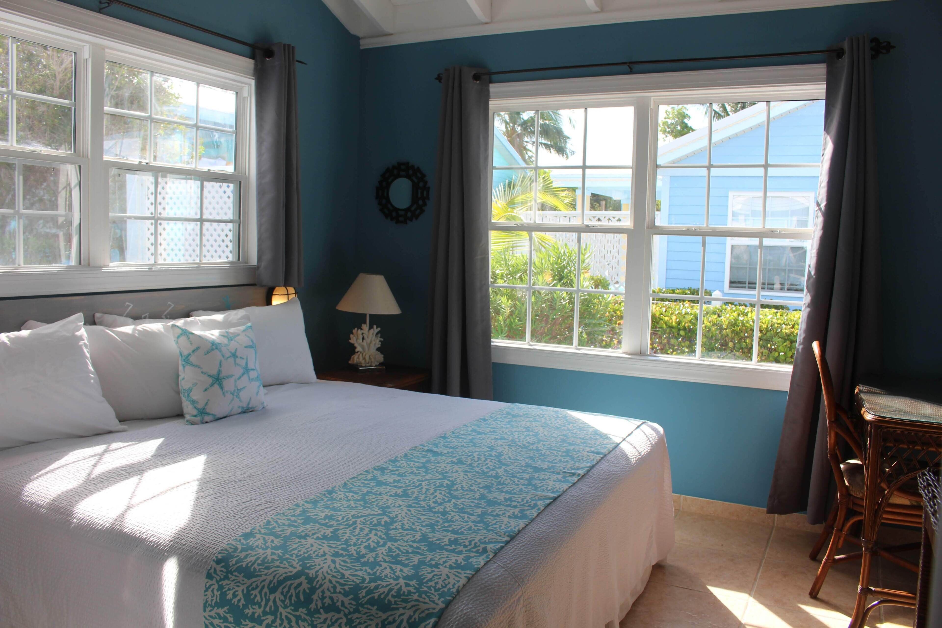 A bedroom with a bed, a nightstand, a chair, a window with curtains, and a view of greenery outside.