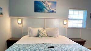 A bed with a white and blue patterned bedspread, a remote control on it, and a painting of a wave on the wall. - HILLSIDE TWO BEDROOM VILLA - OCEANVIEW (Georgetown)
