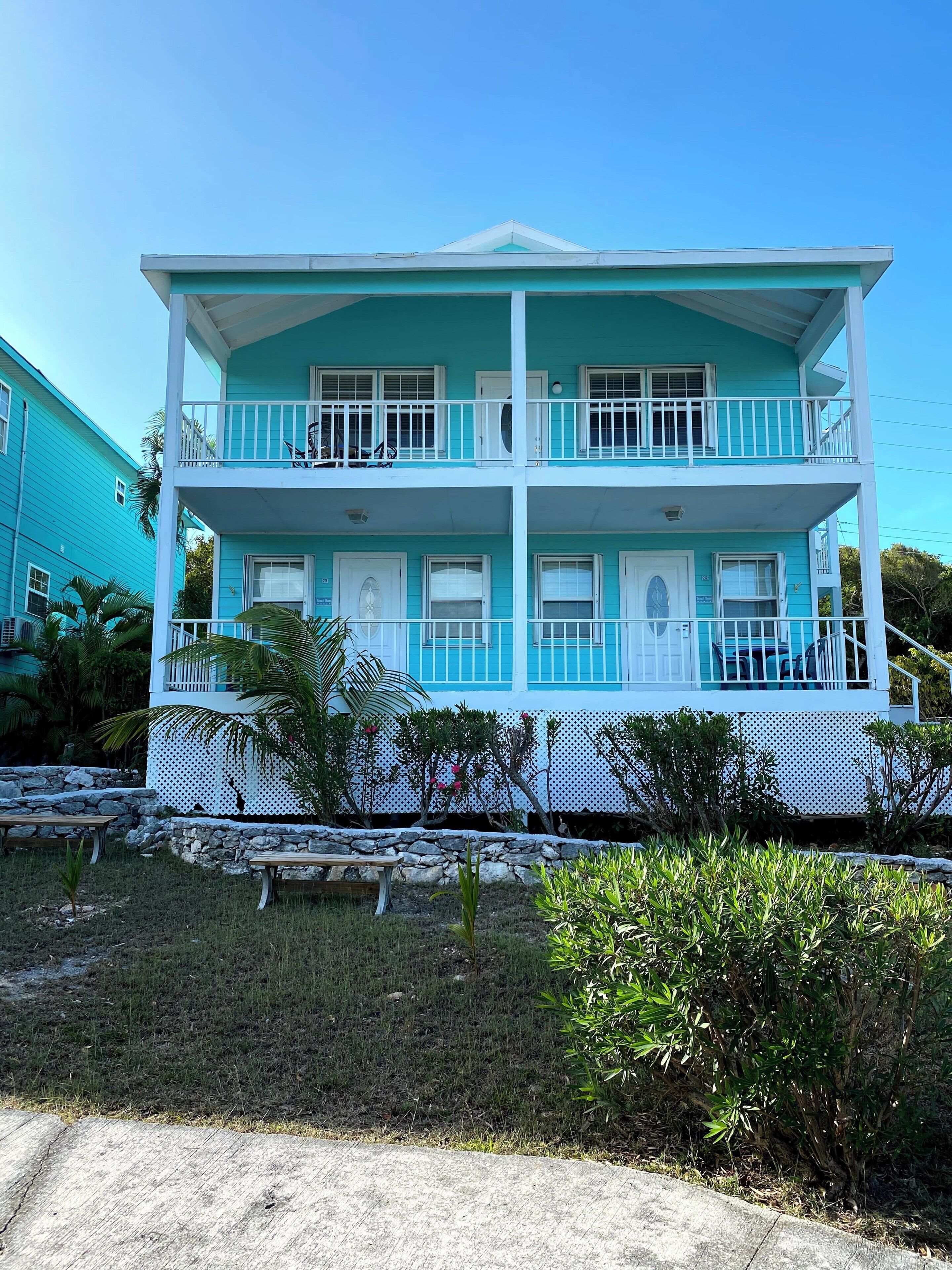 A two-story building with balconies, a stone wall, and a small garden area.
