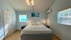 A bedroom with a bed, a ceiling fan, a window with blinds, an air conditioning unit, and a door. - HILLSIDE TWO BEDROOM VILLA - OCEANVIEW (Georgetown)