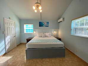 A bedroom with a bed, bedside tables, a ceiling fan, and a window with blinds. - HILLSIDE TWO BEDROOM VILLA - OCEANVIEW (Georgetown)