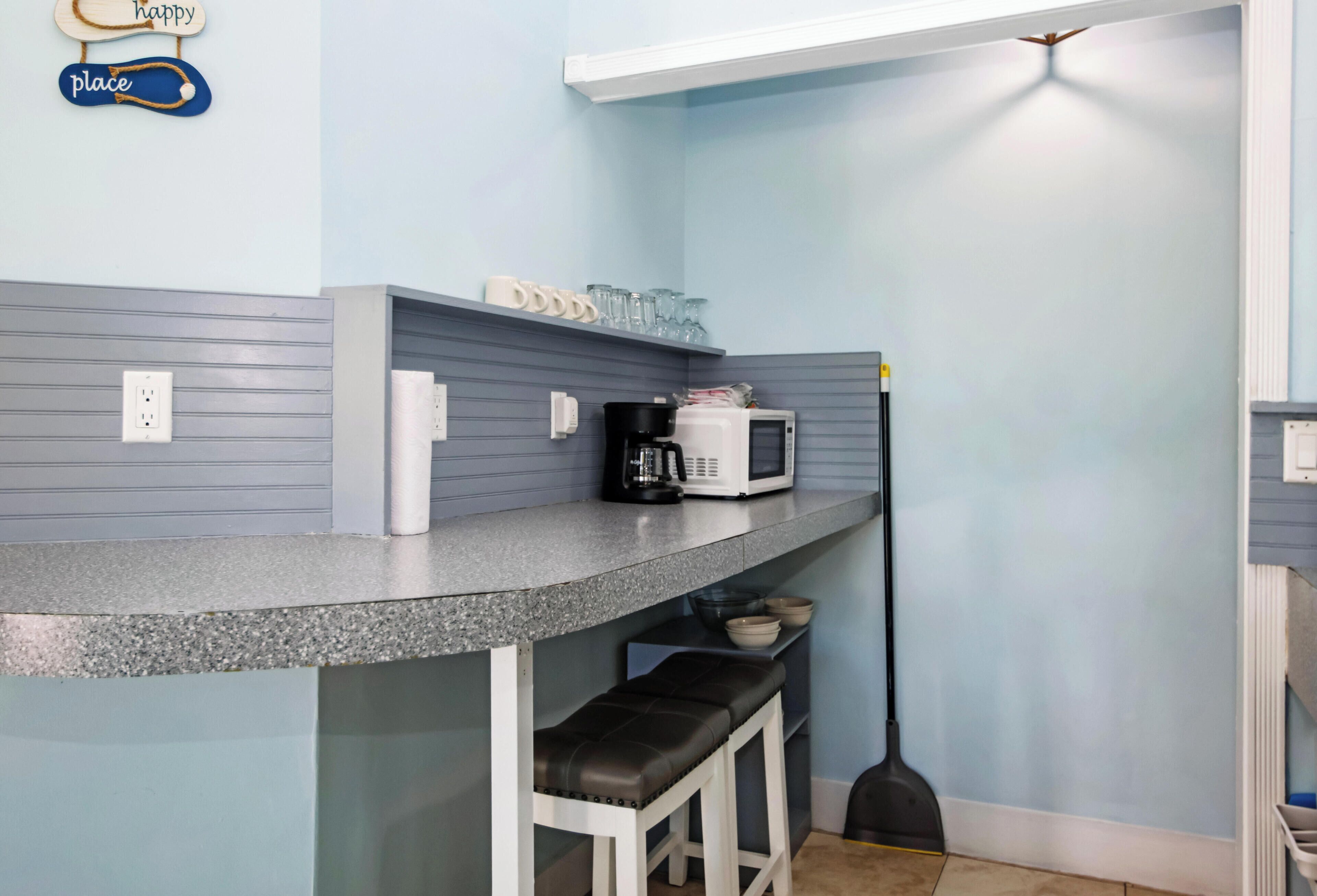 A kitchen with a grey countertop, a coffee maker, a microwave, and a broom.