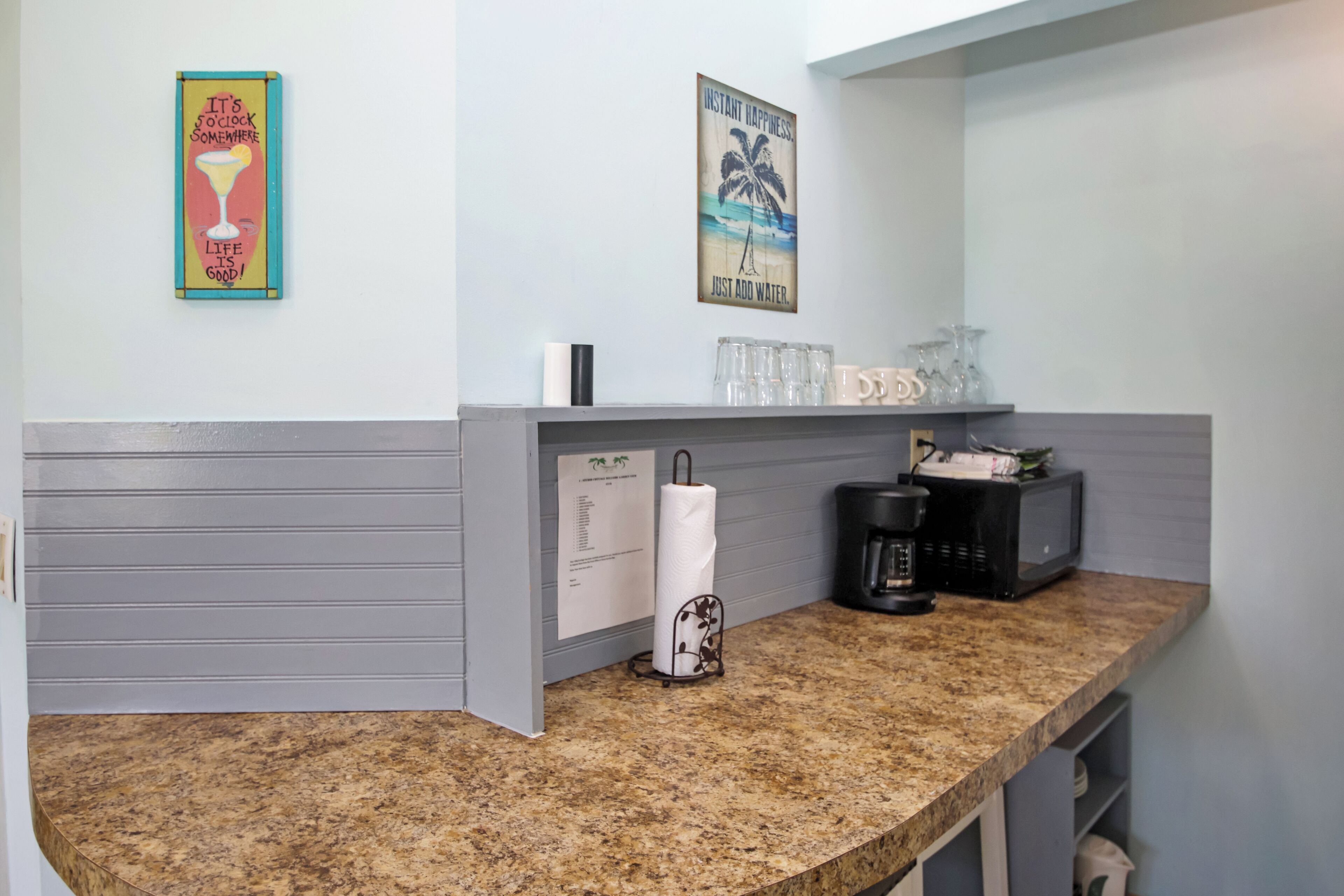 A kitchen counter with a coffee maker, a paper towel holder, and a glass rack.