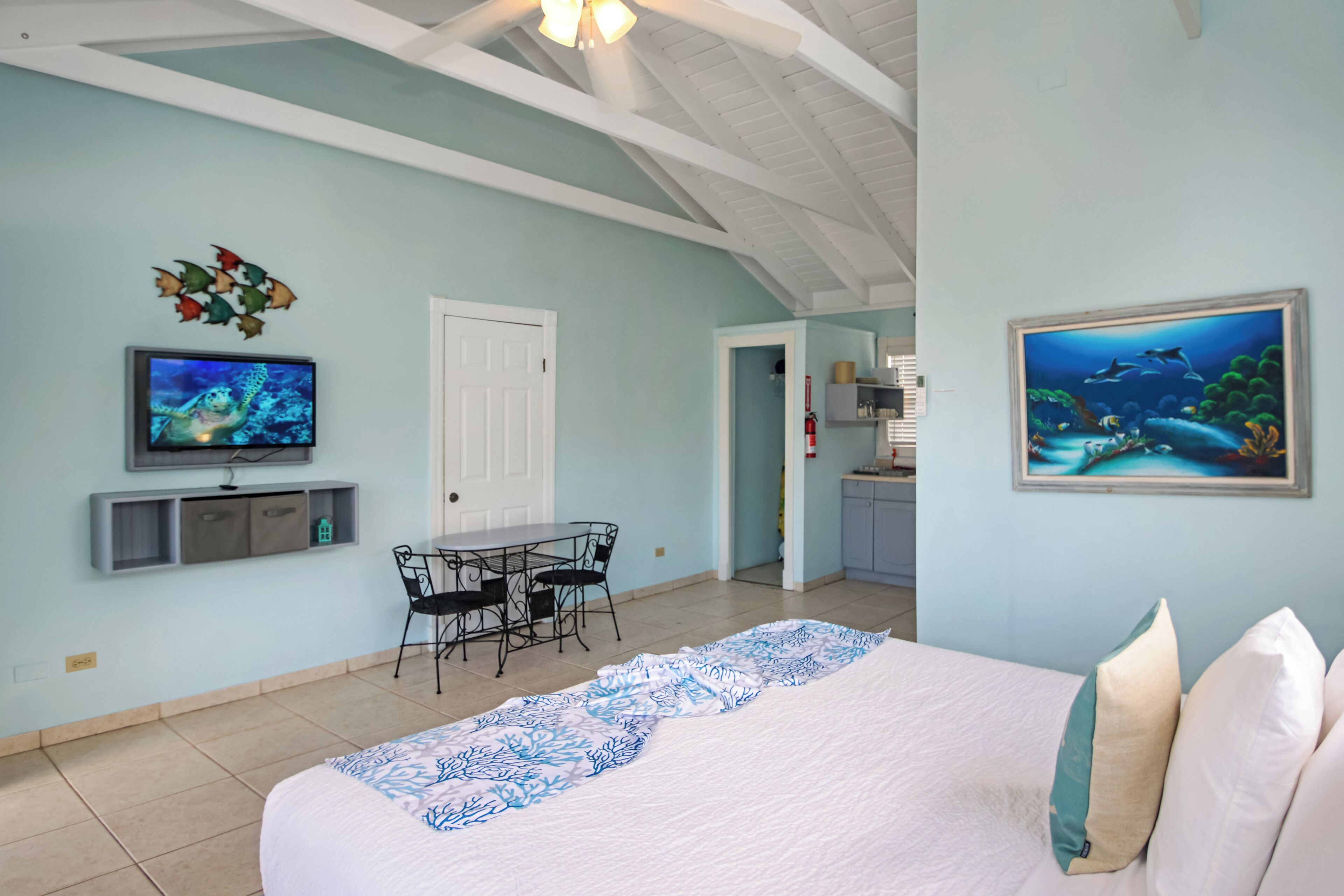 Ein Schlafzimmer mit Bett, Fernseher, Esstisch mit Stühlen, Küchenzeile und Deckenventilator.
