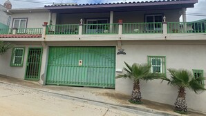A two-story building with a green gate, balconies, and a palm tree. - 9-Bedroom Ocean View Home in Vista Marina for Large Groups (Vista Marina)