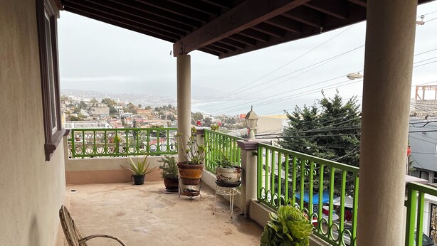 A balcony with a view of a cityscape, potted plants, and wicker furniture. - 9-Bedroom Ocean View Home in Vista Marina for Large Groups (Vista Marina)