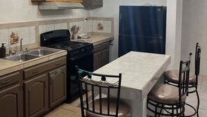 A kitchen with a gas stove, sink, cabinets, and a dining area with chairs and a table. - 9-Bedroom Ocean View Home in Vista Marina for Large Groups (Vista Marina)