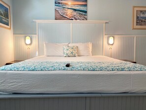 Ein Schlafzimmer mit einem großen Bett, zwei Wandlampen und einem gerahmten Bild mit einer Strandansicht.