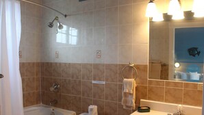 A bathroom with a bathtub, toilet, sink, and a mirror with lights. - BEACHSIDE ONE BEDROOM COTTAGE - OCEANVIEW (Georgetown)