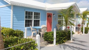 A blue house with a red door, white porch chairs, and a small table. - BEACHSIDE ONE BEDROOM COTTAGE - OCEANVIEW (Georgetown)