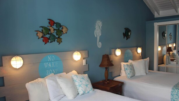 A hotel room with two beds, a 'NO WAKE ZONE' sign, wall art, and a mirror. - BEACHSIDE ONE BEDROOM COTTAGE - OCEANVIEW (Georgetown)