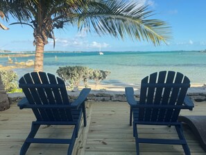 Two Adirondack chairs on a wooden deck overlooking a beach with a palm tree and ocean view. - BEACHSIDE ONE BEDROOM COTTAGE - OCEANVIEW (Georgetown)