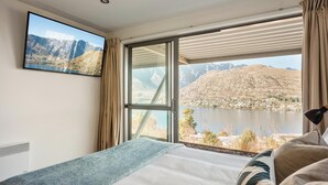 Ein Schlafzimmer mit Bett, Fernseher und einem großen Fenster mit Blick auf Berge und See.
