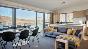 Ein modernes Wohnzimmer mit einem großen Esstisch, schwarzen Stühlen und einem grauen Sofa mit Decke.