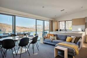 A modern living room with a large dining table, black chairs, and a grey sofa with a throw blanket. - Views on Goldrush, Lake Views, BBQ, Free Parking (Queenstown)