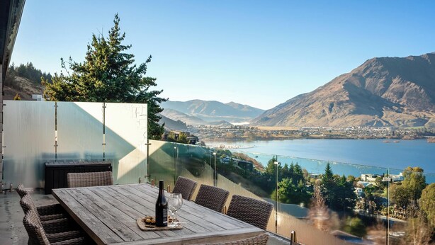 Eine Terrasse mit Tisch und Stühlen, mit Blick auf einen See und Berge.