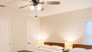 Habitación con dos camas, ventilador de techo, lámparas de noche y suelo de madera.