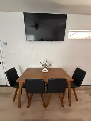 A dining area with a wooden table, black chairs, a small plant, and a mounted flat-screen TV. - Private Guesthouse – Quiet & Cozy (Dallas)