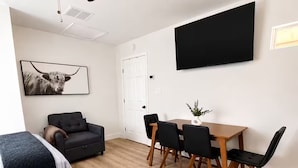 Una habitación con cama, ventilador de techo, mesa de comedor con sillas, sofá y televisor montado.