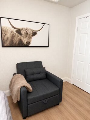 Ein Zimmer mit einem dunkelgrauen Sofa, einer beige farbenen Decke und einem Bilderrahmen mit dem Bild eines Stiers an der Wand.