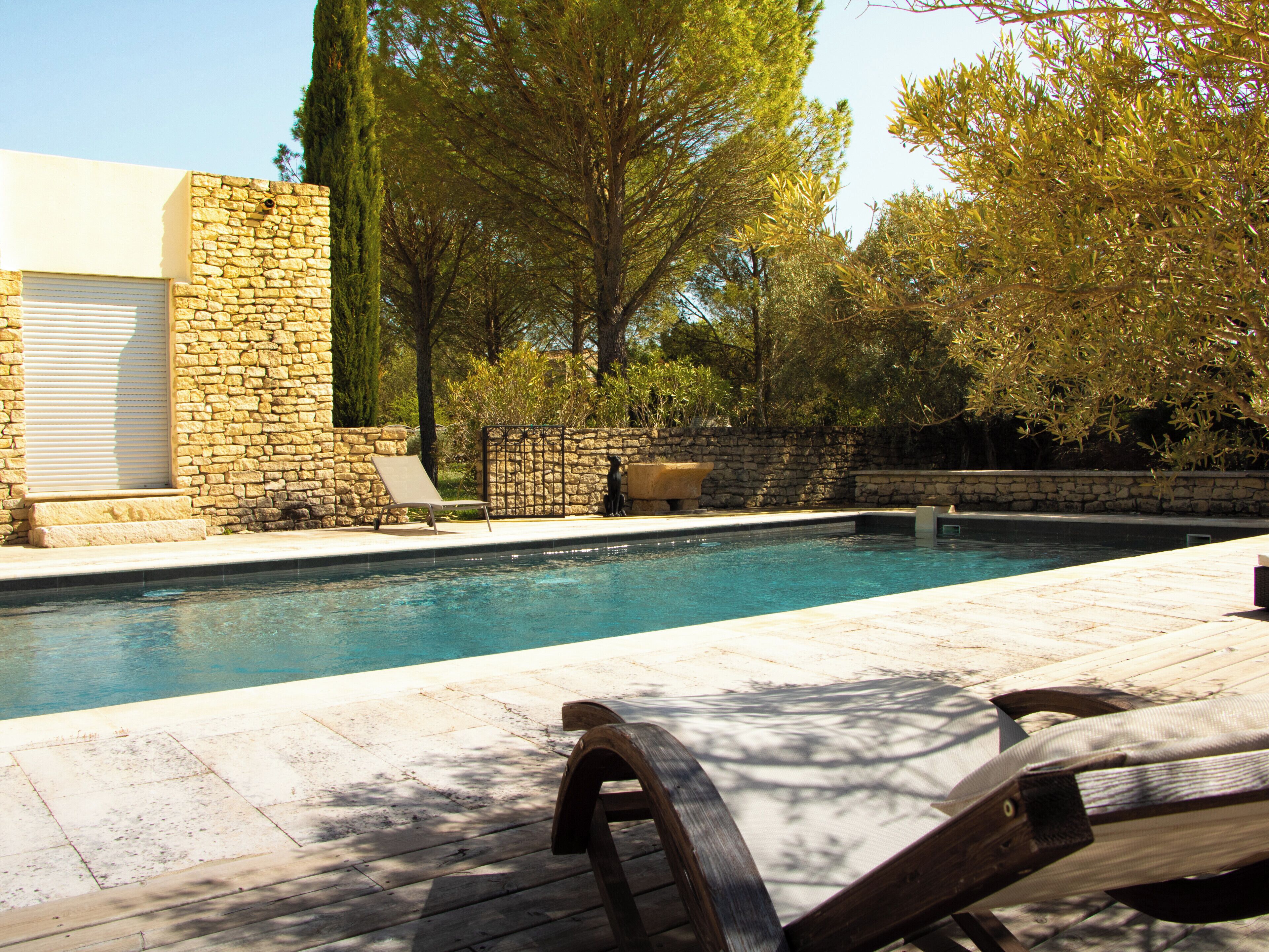 Une piscine avec des murs en pierre, un fauteuil de relaxation et une terrasse en bois.