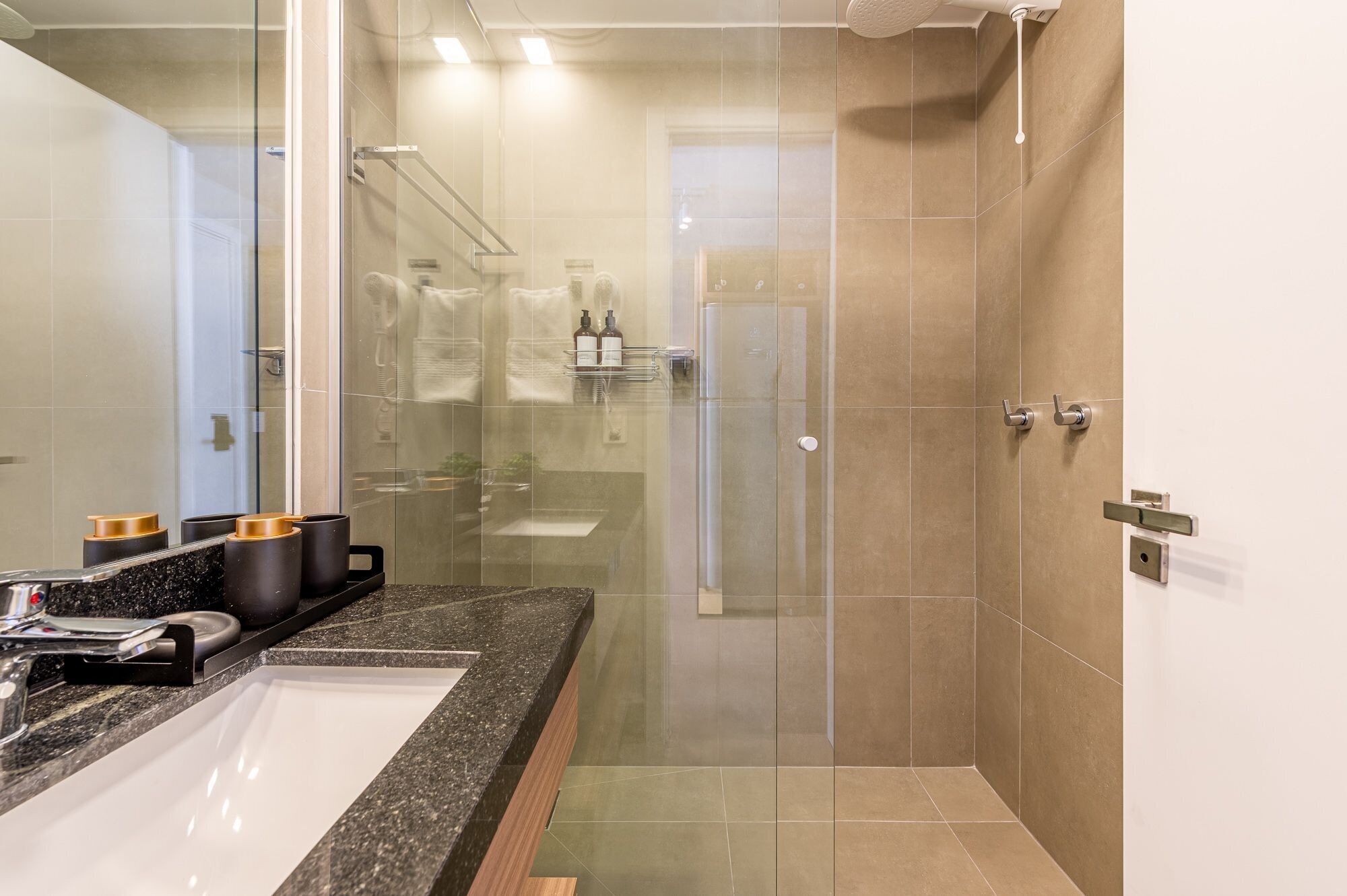 Un baño moderno con ducha envuelta en vidrio, encimera de granito y un espejo grande.