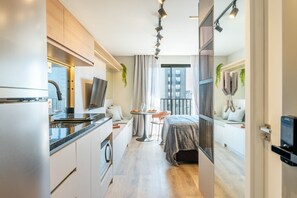 Una habitación de hotel moderna con cocina, zona de comedor y balcón con vista a la ciudad.
