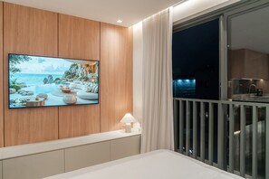 A modern bedroom with a large TV on the wall, a balcony with a railing, and a night view outside. - GO24 by LikeHome (Porto Alegre)
