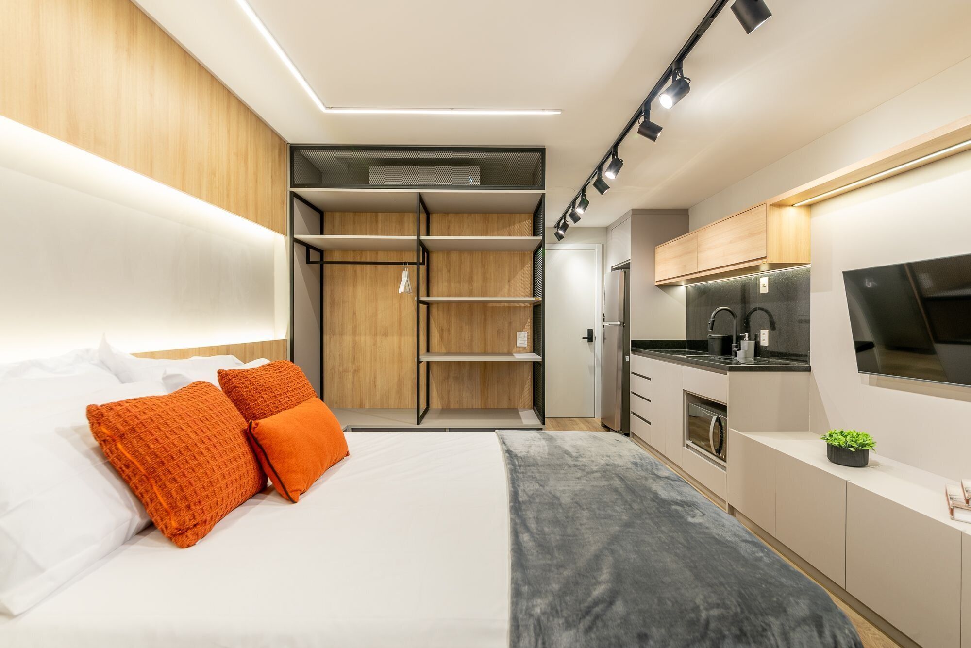 Een knus slaapkamer met een bed, oranje kussens, een kledingkast en een kitchenette met een gootsteen en fornuis.