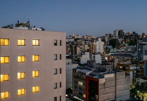 Paisagem urbana ao entardecer, com edifícios que apresentam diversas janelas e uma estrutura vermelha em destaque.