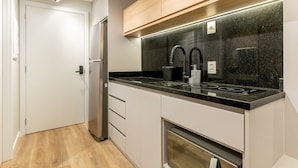 A modern kitchen with a stainless steel refrigerator, a black countertop, a built-in oven, and a wooden upper cabinet.
