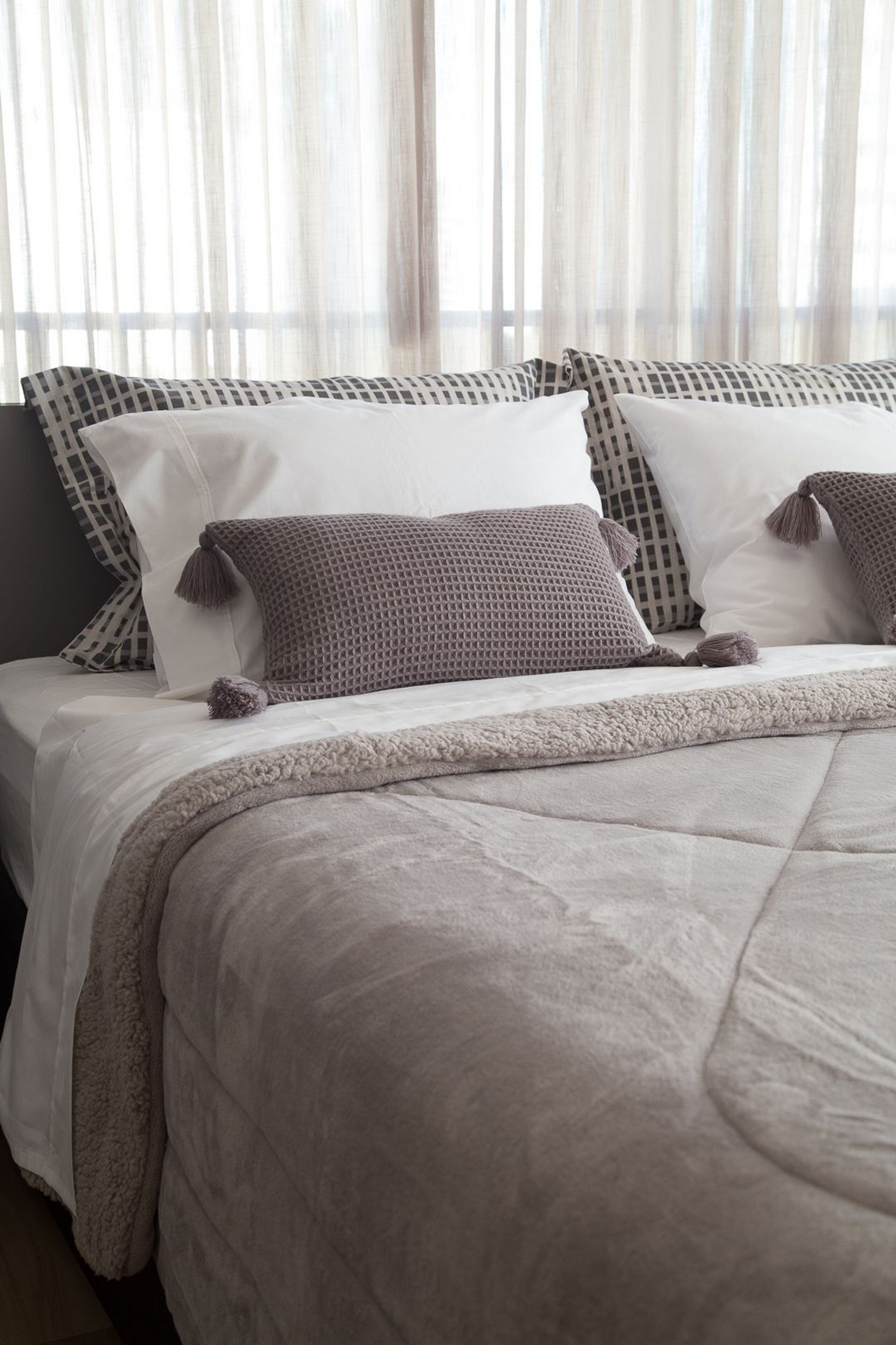 Un lit bien fait, agrémenté d’un coussin à motifs, d’une couverture moelleuse et de rideaux légers en arrière-plan.