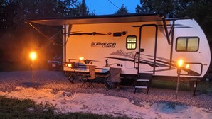 Un camping-car portant l’inscription « SURVEYOR LEGEND », équipé d’une table et de chaises, ainsi que d’une petite structure attenante.