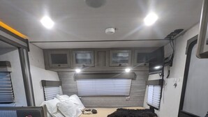 Un intérieur de camping-car compact comprenant un lit, un coin cuisine et des placards de rangement.