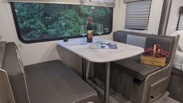 Une petite cuisine équipée avec une table, deux chaises, une bouteille de vin et un panier.