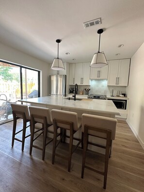 A modern kitchen with a large island, bar stools, and pendant lighting. - Cocoa Beach its Best, Bring FIDO! (Cocoa Beach)